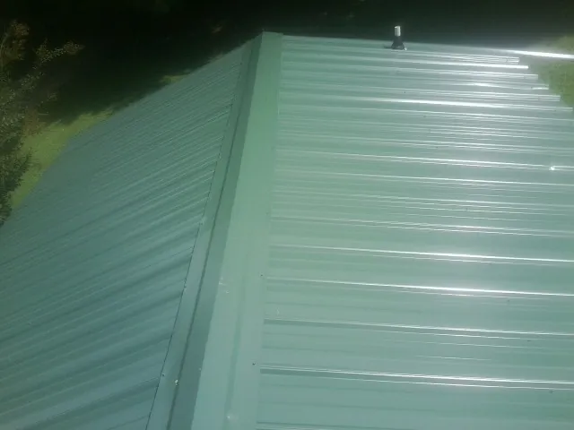 New green metal panels meeting at the ridge of a roof — Flat Roof Repair work by our crew in Auburn